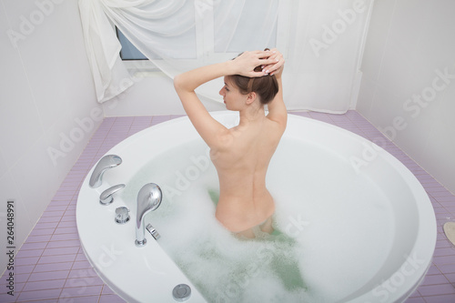 Young pretty woman relaxes in bathtube with soap foam. Spa procedures in bathroom at home or hotelroom. Skin care and moisturizing for youth preservation. photo