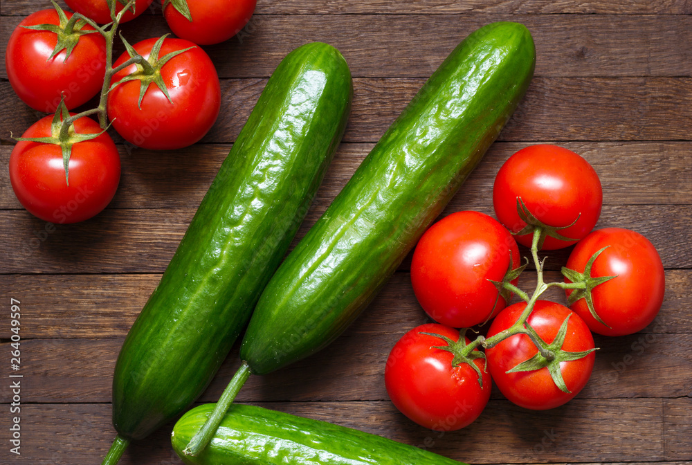 Red ripe tomatoes on branch and big green cucumbers on wooden background.