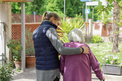 Young carer walking with the elderly woman in the garden