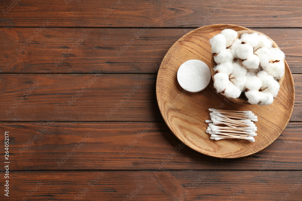 Plate with cotton swabs, pads and flowers on wooden background, top view. Space for text Plate with cotton swabs, pads and flowers on wooden background, top view. Space for text