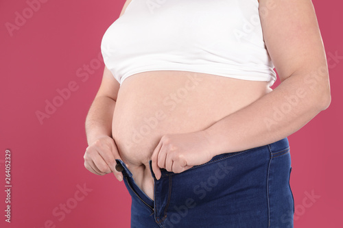 Overweight woman trying to wear tight jeans on color background, closeup © New Africa