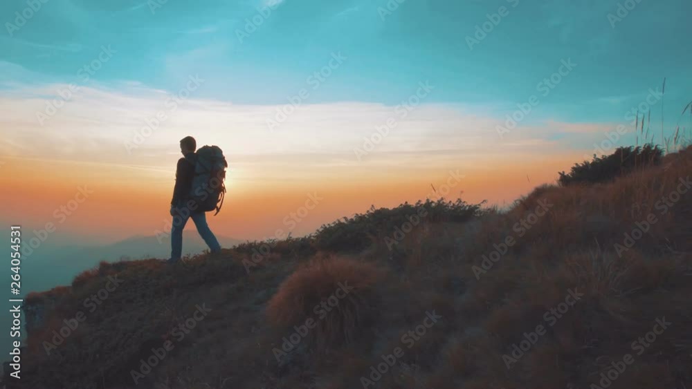 The man with a tourist backpack walking on a mountain on a sunset background The man with a tourist backpack walking on a mountain on a sunset background