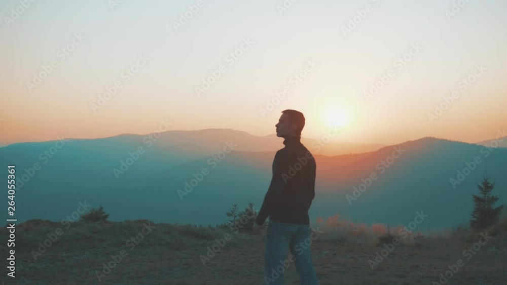 The man stands near the camping tent on the mountain on a sunset background The man stands near the camping tent on the mountain on a sunset background