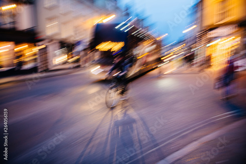 Abstract defocused light-trails of fast cyclist silhouette delivering food ordered through mobile app - fast double-decker bus behind © ifeelstock