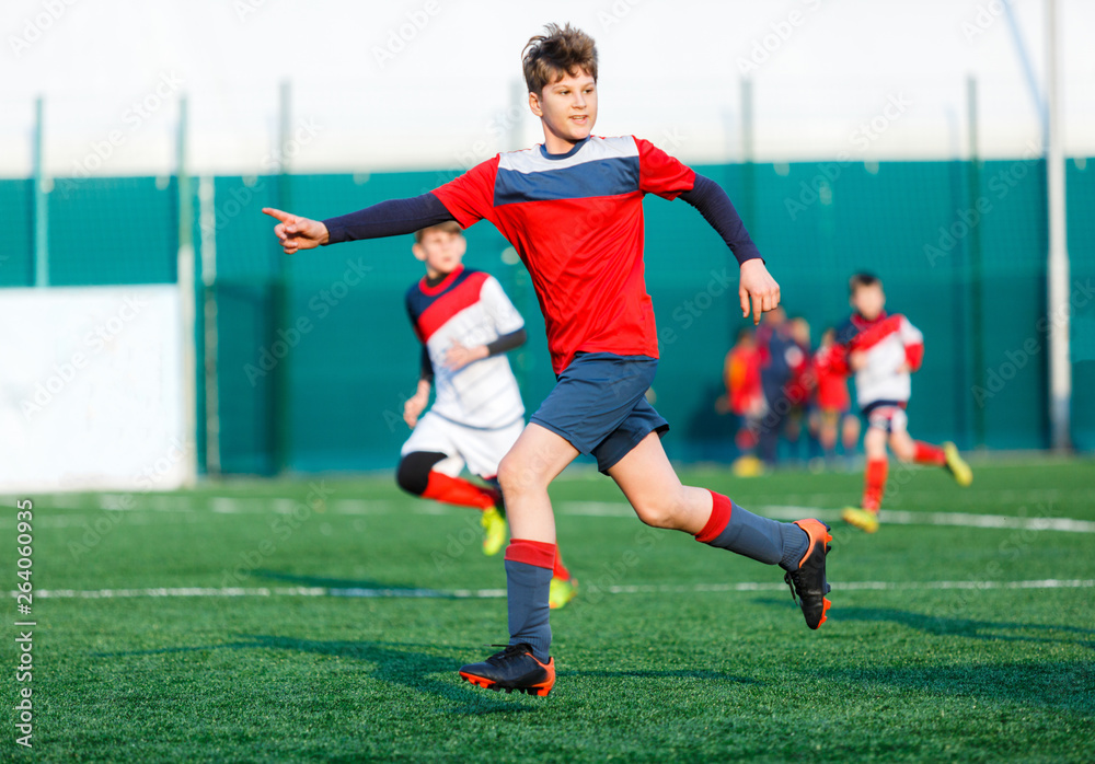 Boys at white red sportswear run, dribble, attack on football field. Young Soccer players with ball on green grass. Training, football, active lifestyle for kids  