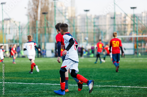 Boys at white red sportswear run, dribble, attack on football field. Young Soccer players with ball on green grass. Training, football, active lifestyle for kids   © Natali