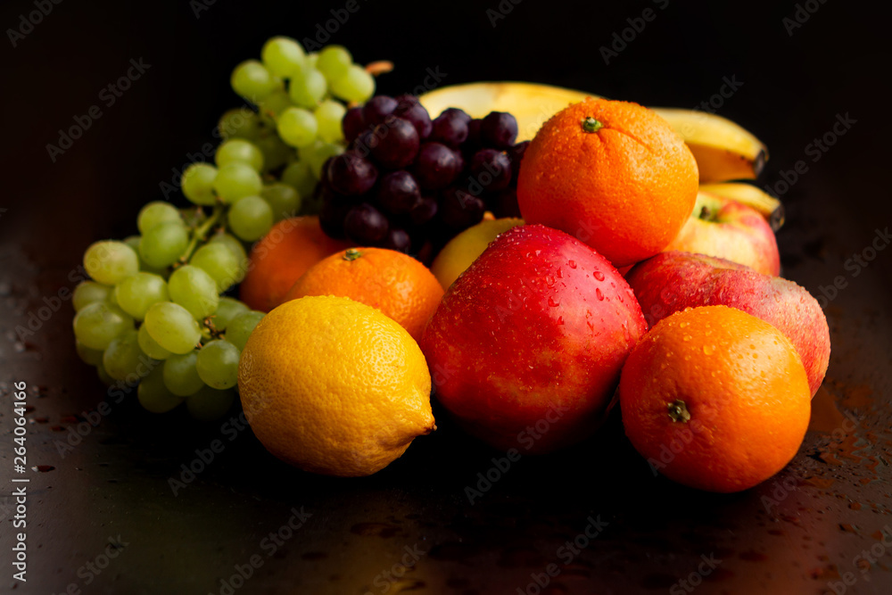 Beautiful juicy fruits on a black wet background: apples, grapes, oranges, bananas, copy space, close-up Beautiful juicy fruits on a black wet background: apples, grapes, oranges, bananas, copy space, close-up