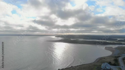 Cinematic drone / aerial footage moving backwards showing a road by the ocean, a chalet and waves hitting the beach at Cole Harbour coast in Lawrencetown, Nova Scotia, Canada during summer season. photo