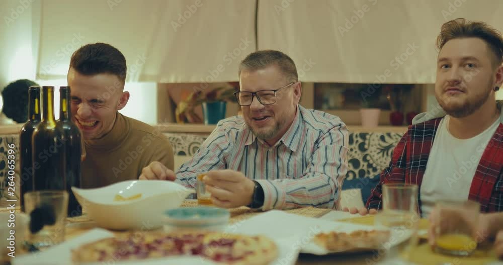 Men's company is resting, eating pizza and laughing. Friends communicate at the table and celebrate the holiday. Men's company is resting, eating pizza and laughing. Friends communicate at the table and celebrate the holiday.