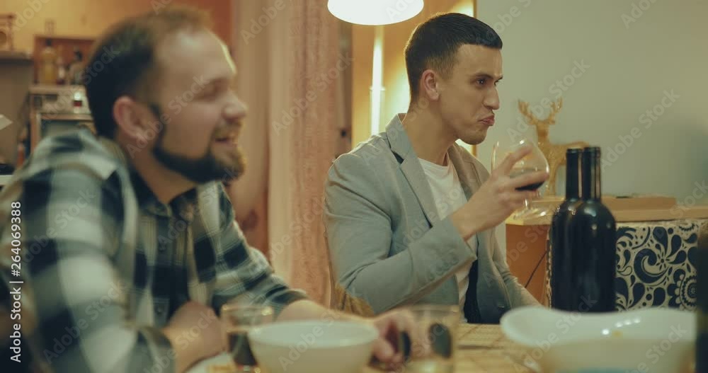 Nice guy drinks wine from a glass, laughs and talks among friends. Friendly party in a cozy interior. Merry company notes meeting. Nice guy drinks wine from a glass, laughs and talks among friends. Friendly party in a cozy interior. Merry company notes meeting.