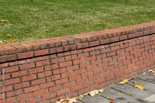 Brick retaining wall with dirt stained mortar, green grass and concrete, horizontal aspect