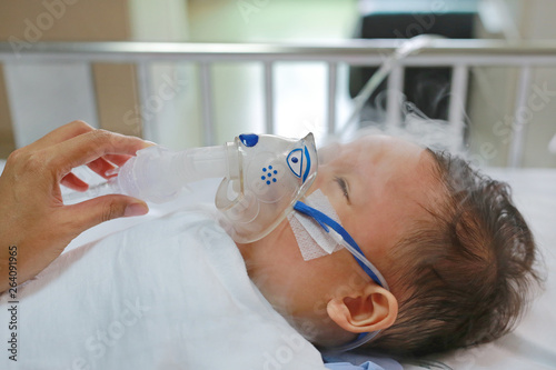 Toddler boy using nebulizer to cure asthma or pneumonia disease . Sick baby boy rest on patients bed and has inhalation therapy by the mask of inhaler. Respiratory Syncytial Virus (RSV). photo
