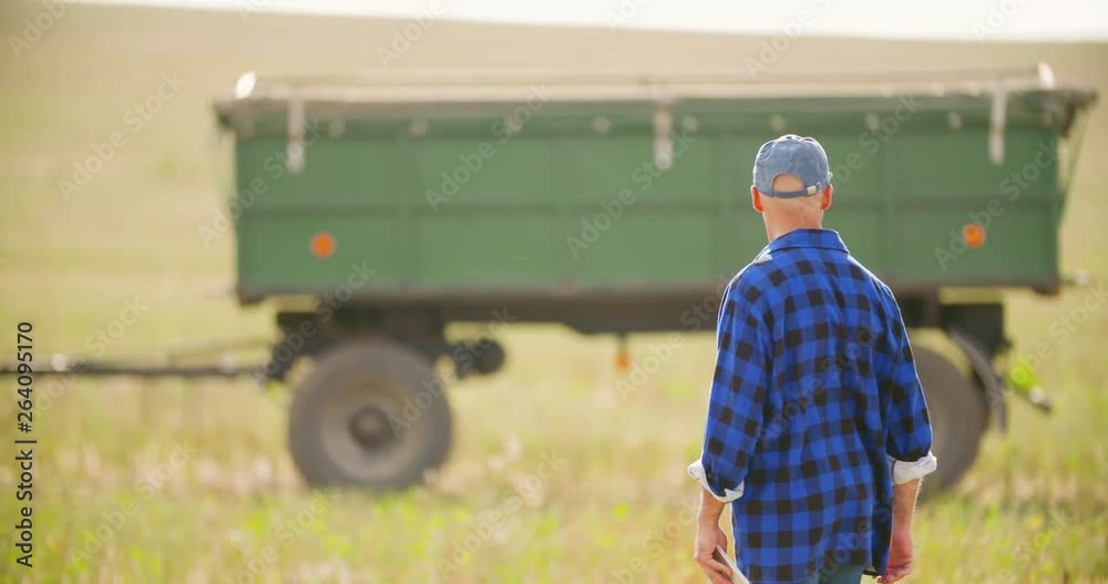 Farmer using digital tablet while looking at tractor in farm Farmer using digital tablet while looking at tractor in farm