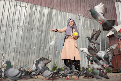 Photography young happy Muslim woman in hijab feeds pigeons