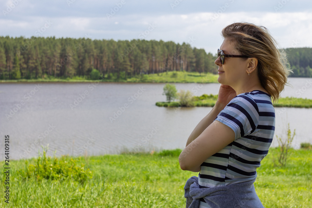 An adult happy woman stands on the shore of the lake, enjoying nature.