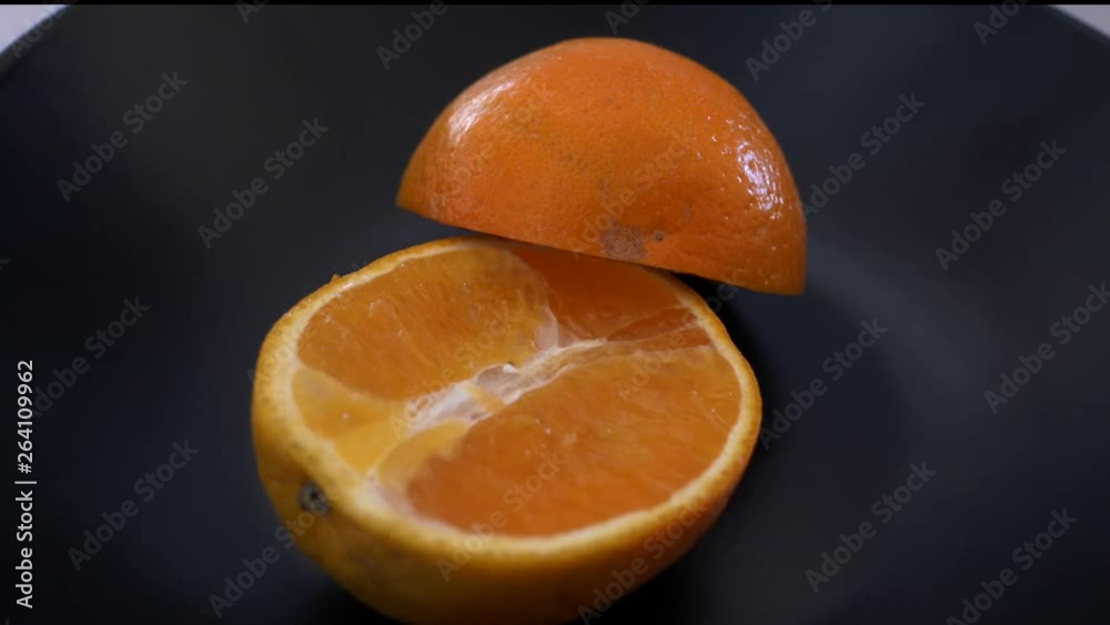 Slow motion pan around cut in half orange on a black plate Slow motion pan around cut in half orange on a black plate