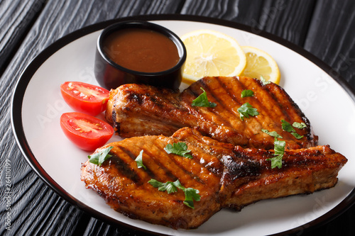 Freshly prepared grilled pork steak with tamarind sauce, lemon and fresh tomatoes close-up on a plate. horizontal