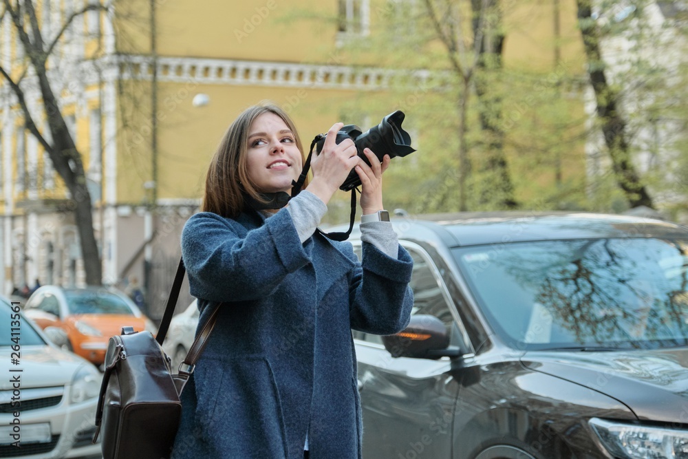 Beautiful young woman with camera in city. Tourist girl traveling and photographing, spring city street background