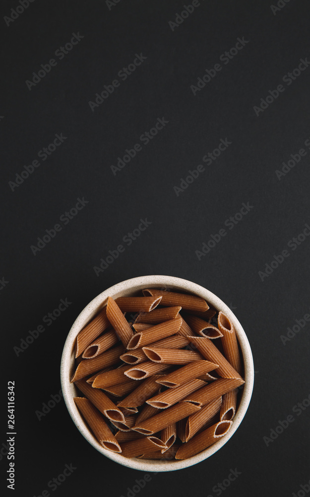 Whole grain macaroni on dark background, vertical, free space for text, top view Whole grain macaroni on dark background, vertical, free space for text, top view