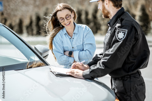 Policeman issuing a fine for violating the traffic rules to a young woman driver while standing near the car on the roadside