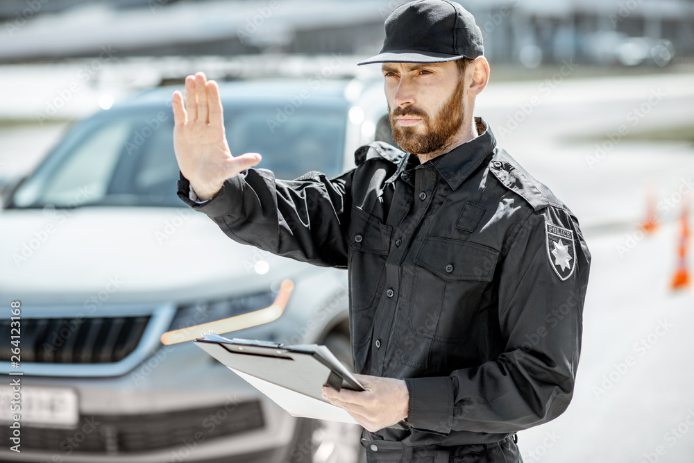 Portrait of a handsome policeman in uniform standing in front of a car on the roadside Portrait of a handsome policeman in uniform standing in front of a car on the roadside