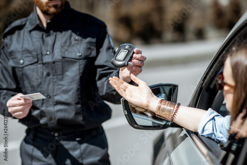 Policeman checking woman driver for alcohol intoxication with special device while stopped for violation traffic rules on the roadside