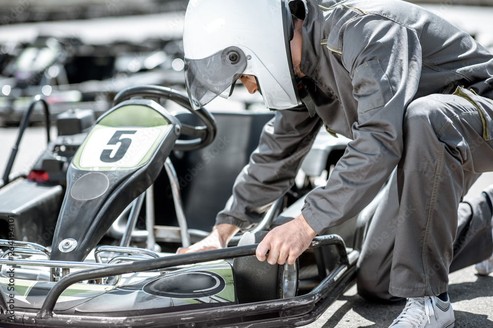 Racer or repairman in uniform serving go-kart machine before racing on the track Racer or repairman in uniform serving go-kart machine before racing on the track