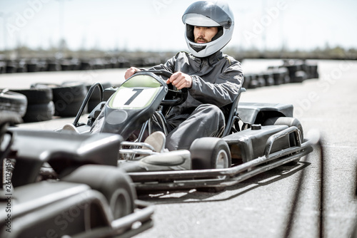 Racer in sportswear and protective helmet driving go-kart on the track