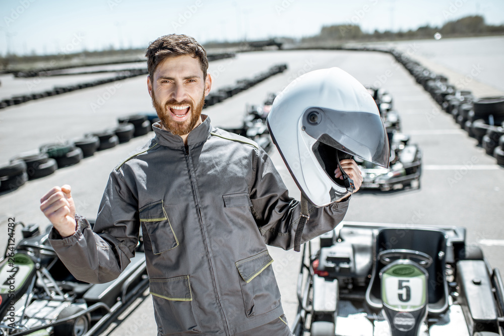 Portrait of a happy racer in protective sportswear standing as a winner of a go-kart race outdoors