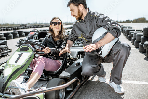 Man in sportswear instructing young woman driver before racing on the go-karts on the track outdoors