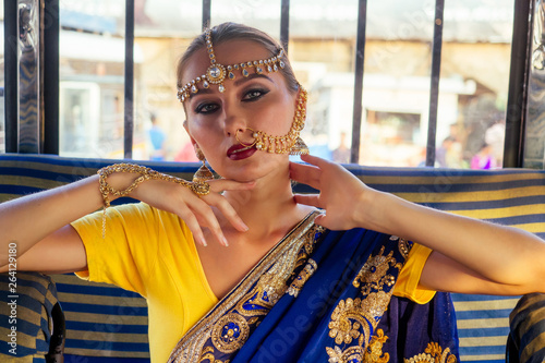 portrait indian beautiful Caucasian woman in traditional blue dress.hindu model with golden kundan jewelry set bindi earrings and nose ring piercing nath fashion photoshoot on the street market