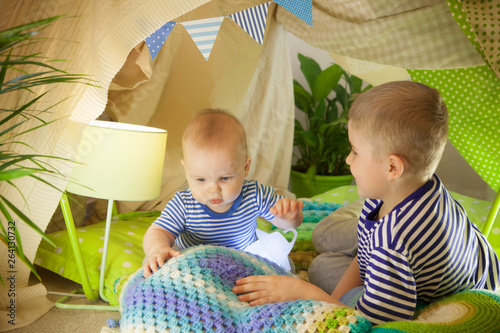 Two cute brothers play with a flashlight in a children's tent. 6 years old boy and baby toddler