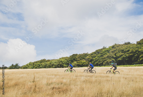 Mountain bikers ride together through grassland field in English countryside