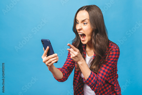 Portrait of a furious young business woman yelling at mobile phone isolated over blue background.