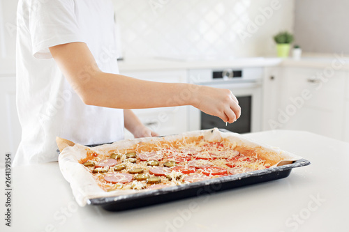 Cooking concept - cook manually adding grated cheese to pizza in the home kitchen. Close-up