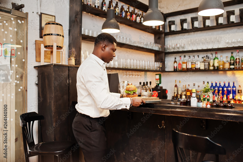 Young african american waiter man hold tray with burger at bar of restaurant. Young african american waiter man hold tray with burger at bar of restaurant.