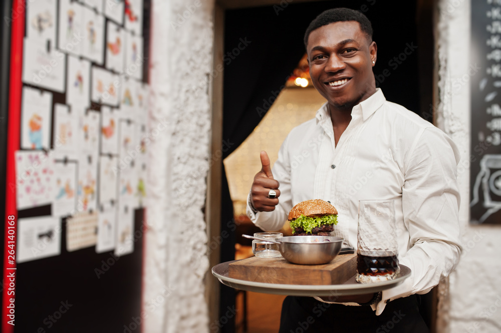 Young african american waiter man hold tray with burger at restaurant and show thumb up.
