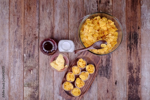 Bowl with cornflakes, conflakes cup, suger, butter and honey on  wooden background