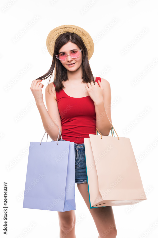 Portrait of a cheerful young woman in summer hat and sunglasses holding shopping bags isolated over white background Portrait of a cheerful young woman in summer hat and sunglasses holding shopping bags isolated over white background
