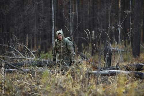 Man in camouflage overcomes a windbreak in an autumn forest. Extreme travel. Survival in the wild.