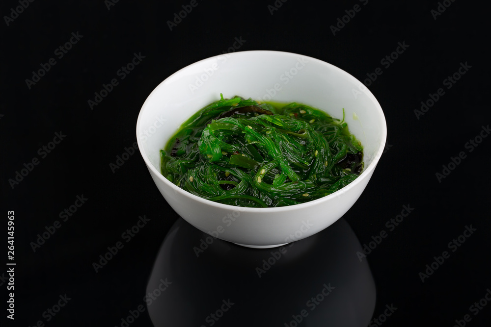 Salad with seaweed and sesame in the dark plate in the center of the black background. Salad with seaweed and sesame in the dark plate in the center of the black background.