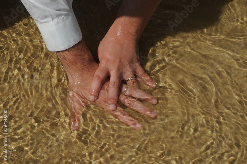 hands of bride and groom with wedding ring in the sand