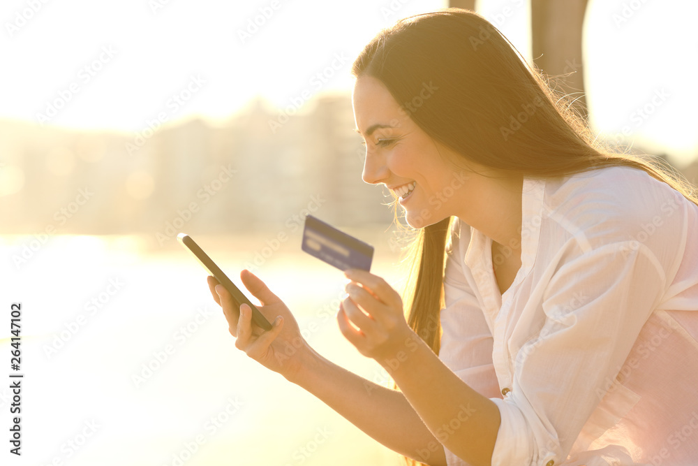 Happy woman pays online with credit card at sunset