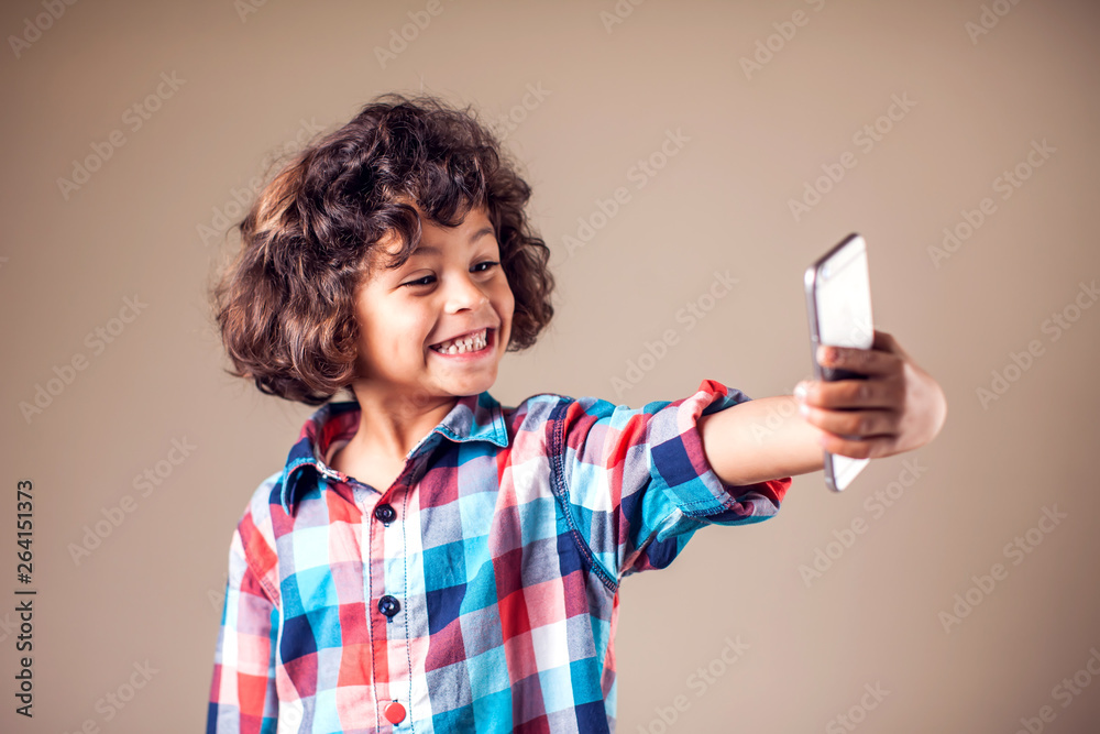 Kid having fun and taking selfie with cell phone over grey background. Children and technology concept Kid having fun and taking selfie with cell phone over grey background. Children and technology concept