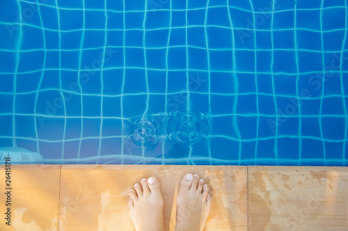 Top view of bare female foot standing beside the edge of blue swimming pool with wave on the sunny day