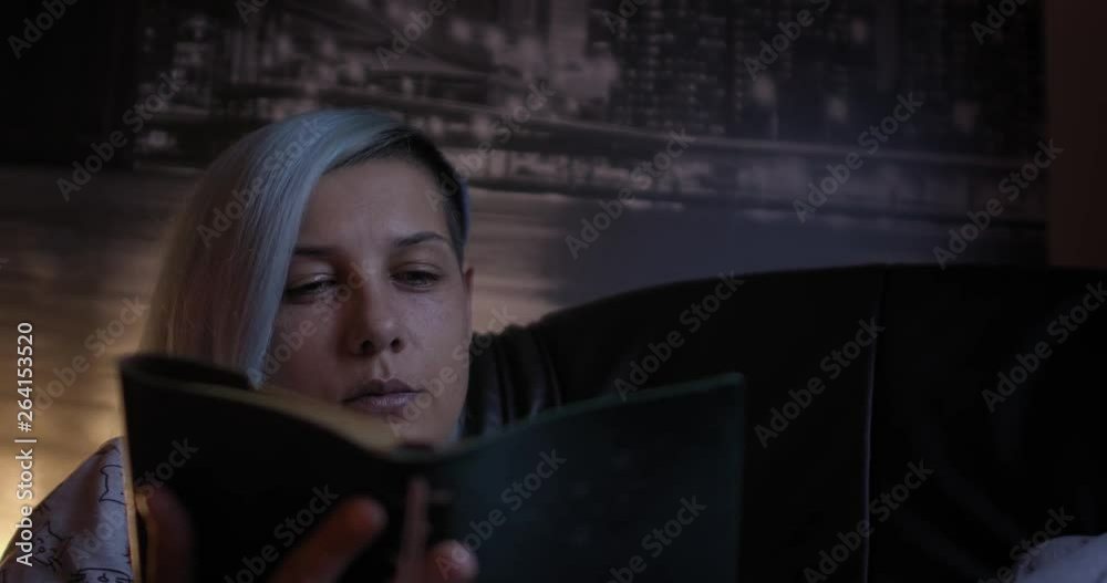 Young woman relaxing and reading an old book in dark and cozy room; with blue hair; close up.