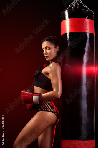 Young woman sportsman boxer doing boxing training at the gym. Girl wearing gloves, sportswear and hitting the punching bag. Isolated on black background with smoke. Copy Space.