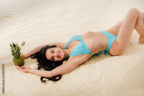 beautiful smiling girl in Bikini holding pineapple and resting on sandy beach