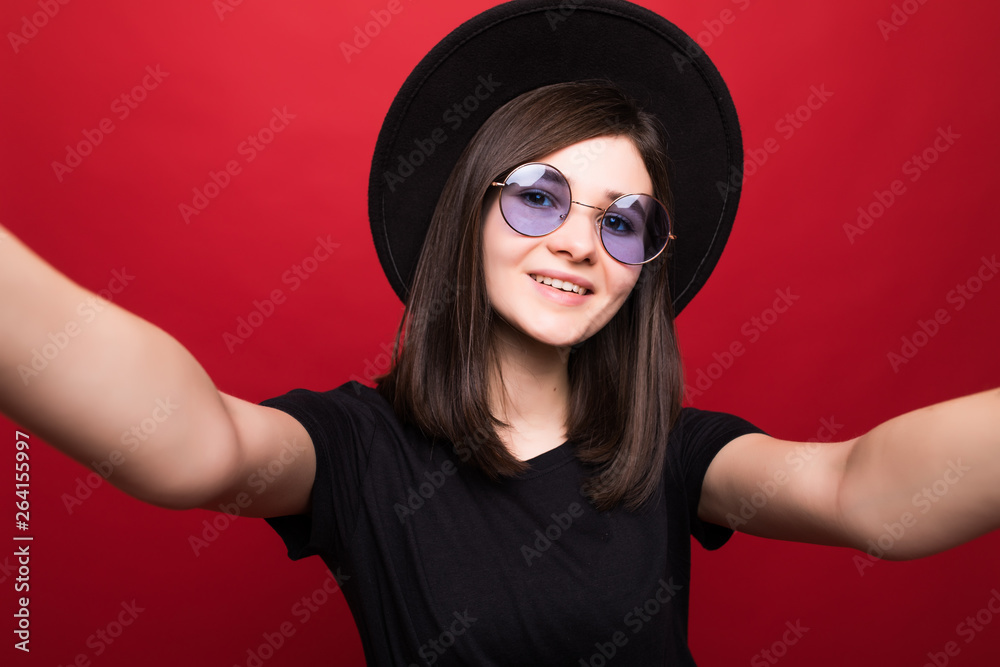 Fashion hipster woman taking selfie. Black hat, leather jacket, sunglases, bright red lips. Trendy fashion style