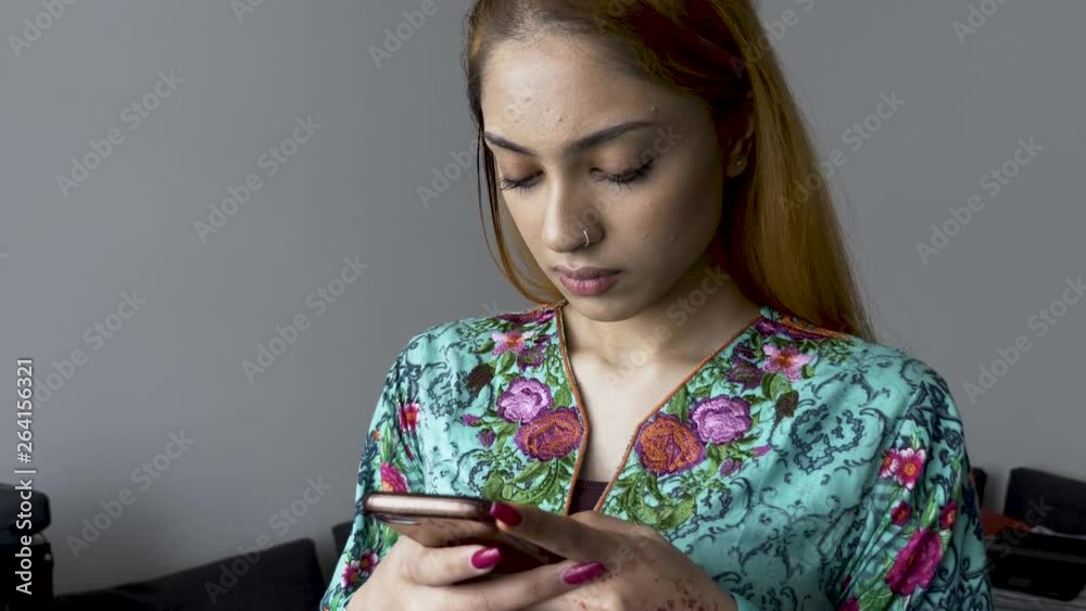Young Asian Indian female in colourful salwar kameez checking smartphone standing up indoors Young Asian Indian female in colourful salwar kameez checking smartphone standing up indoors